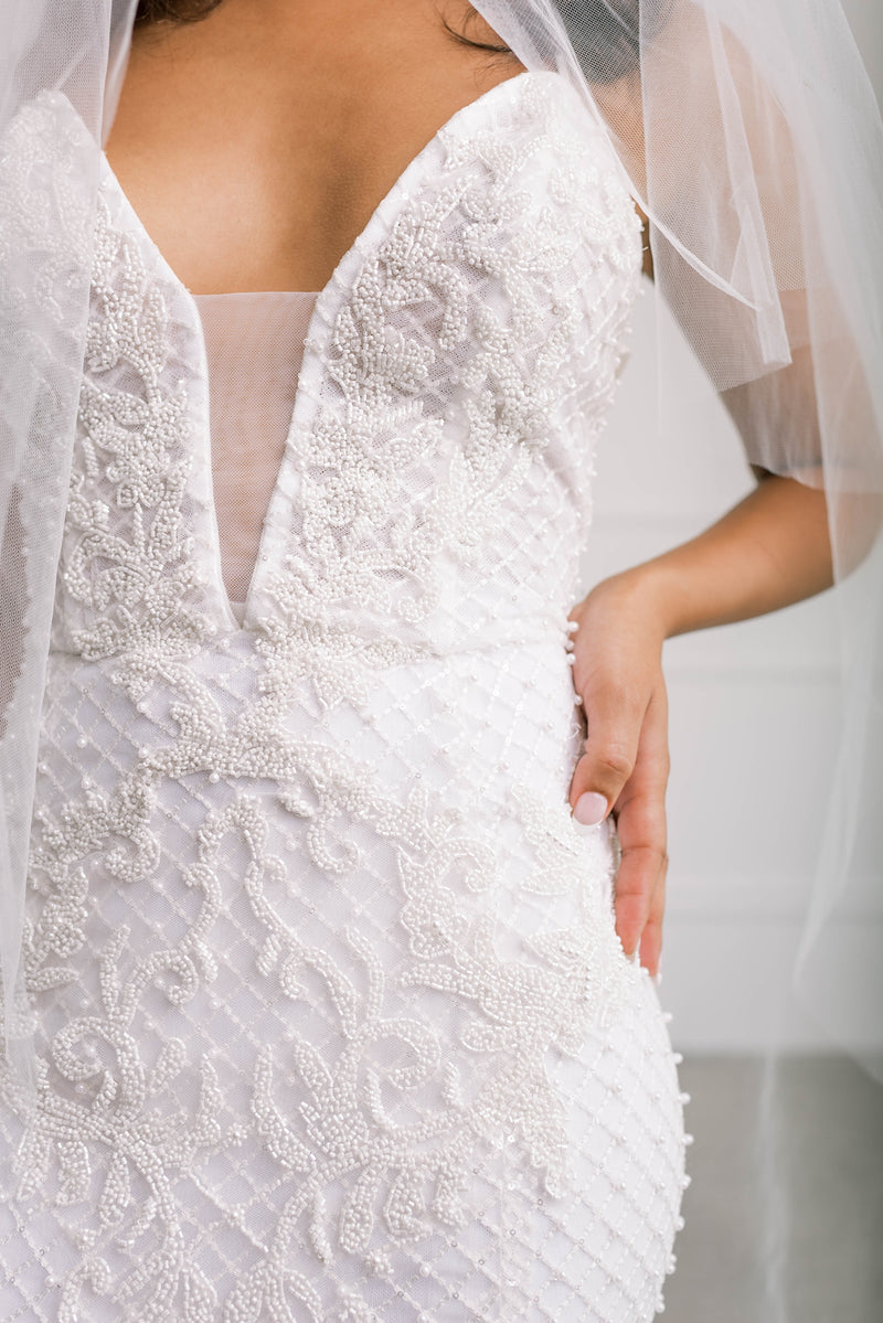 Up close custom beading detail on ivory wedding dress with plunging neckline