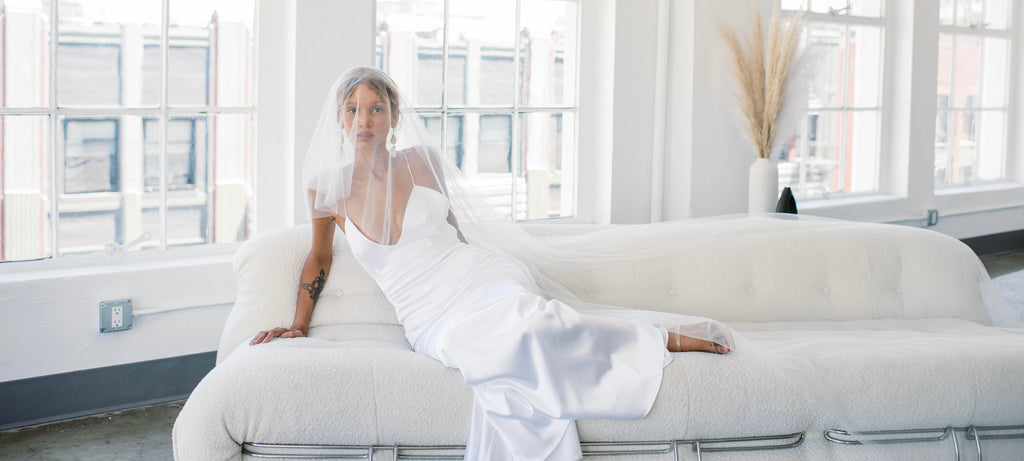 Graceful bride sitting on modern white couch wearing glamourous hollywood dress 