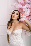 Glamorous bride wearing a luxury Swarovski crystal choker cape, with stunning jewel studded detailing, next to pink flowers